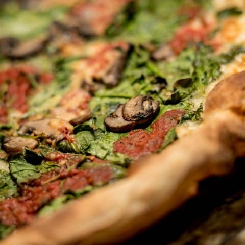 Close-up view of a veggie pizza with crispy crust, mushrooms, and spinach