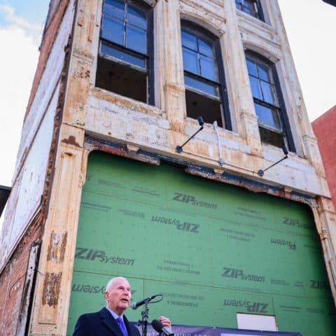 Man stands at podium giving speech outside of apartment building in development