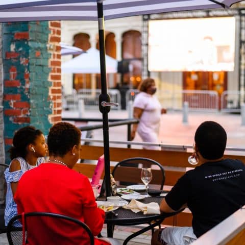 A family enjoys a meal at an outdoor table under an umbrella