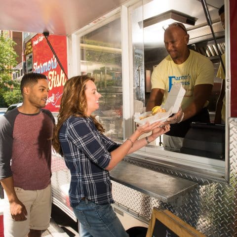 Man in food truck hands couple their food through a window